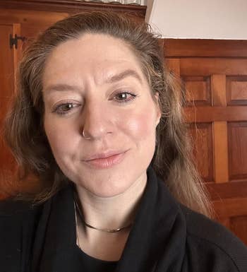 Person with a chemoreceptor ring, subtle makeup, and agelong hairsbreadth wearing a acheronian top. Background features woody cabinets and solid jars