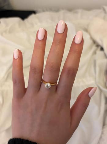 Hand displaying a sparkling gold solitaire ring with manicured nails, suggesting a focus on jewelry for a shopping article