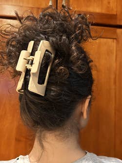 A person with curly hair styled in an updo using a large claw hair clip, shown from the back against a wooden background