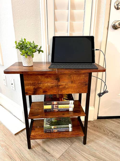 reviewer's wooden side table with shelves holding books, a potted plant, and tablet