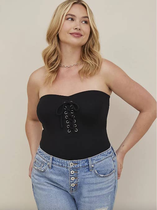 model in black strapless top with lace up front detail tucked into jeans
