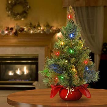 the lit-up mini tree on a table in front of a fireplace