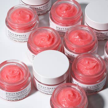 Multiple Alpyn Beauty lip balms, some with their tops off to showcase the creamy pink texture