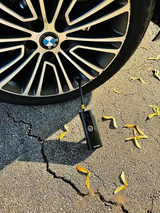 Portable tire inflator connected to a car’s tire on a cracked pavement with scattered leaves