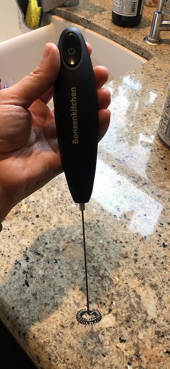 Reviewer holding black hand frother with silver whisk over counter