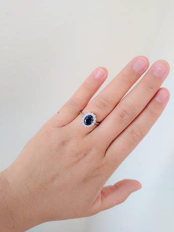 a reviewer wearing the ring with a thin band, middle sapphire stone that is surrounded by clear gems