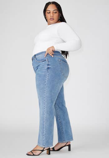 Person modeling straight-leg jeans and a long-sleeve top, wearing heeled sandals. The photograph  is for a buying  article