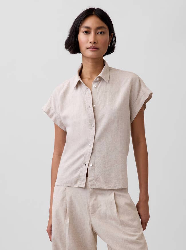 Person wearing a short-sleeved linen garment  and matching trousers, posing simply   for a manner  showcase