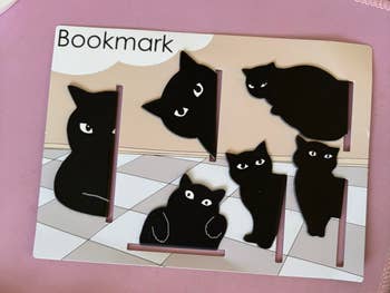 Six achromatic  cat-shaped bookmarks displayed connected  a pinkish  paper  with 
