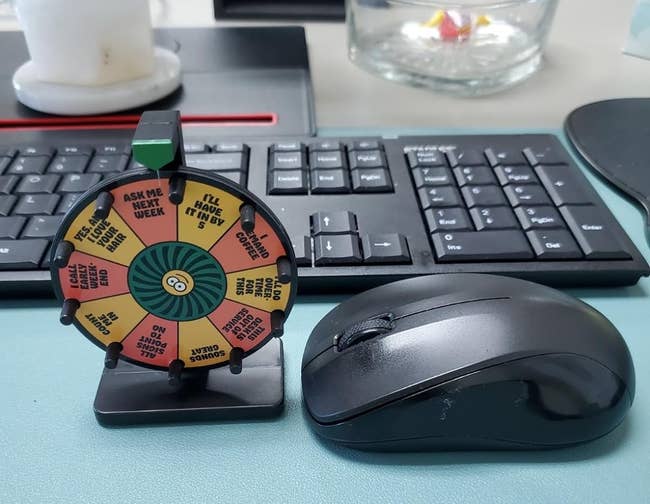 Decision-making wheel on desk next to keyboard and mouse; can be spun to give answers for office choices