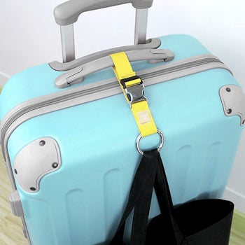 The yellow luggage strap attached to a rolling suitcase holding a tote bag