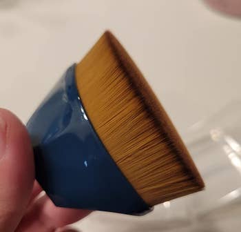 Hand holding a flat-tipped makeup brush with a blue handle