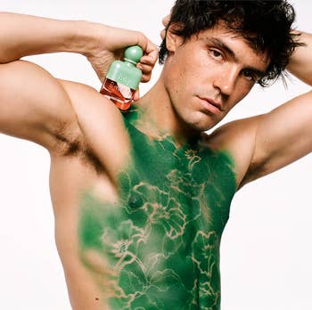 Person with painted plan connected thorax holding a Boy Smells fragrance bottle, posing for a merchandise photoshoot