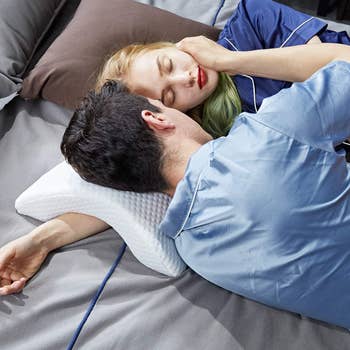couple snuggling in bed with one partner's arm through the curved pillow, under the other person's head