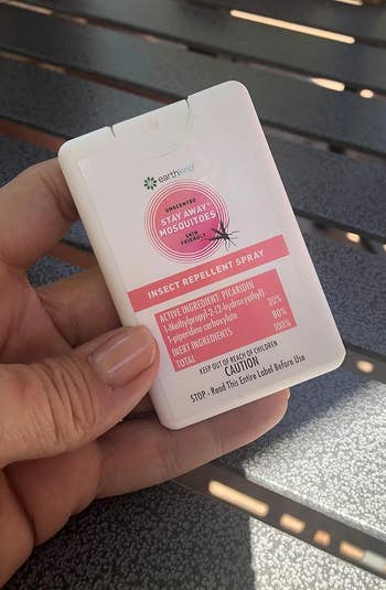 Hand holding a card-sized insect repellent spray bottle with product details