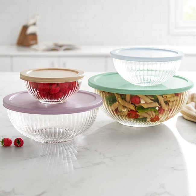Set of glass storage bowls with lids on a kitchen counter, filled with pasta salad and berries, suitable for food storage and meal prep
