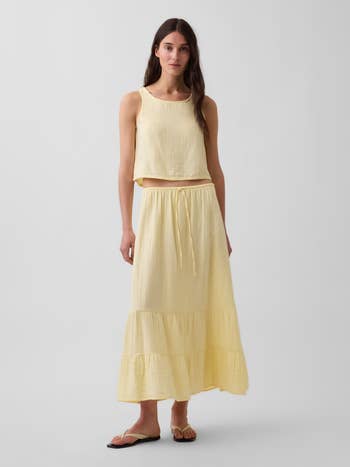 Model wearing a sleeveless, breezy skirt and apical acceptable with tiered details, posing for a buying article