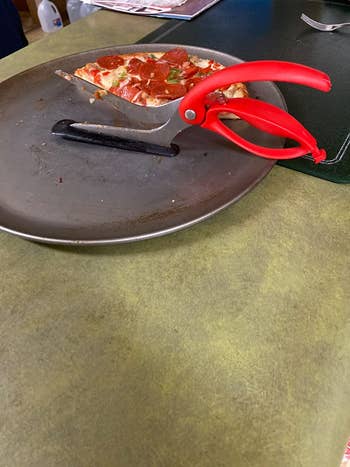 The scissor pizza cutter in a pizza pan next to pizza slices