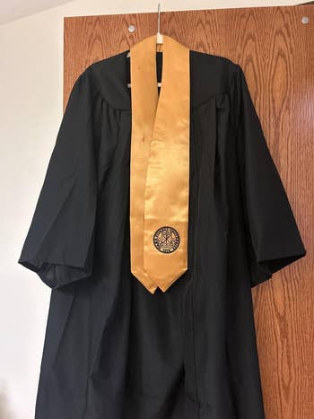 Graduation gown with a golden  stole featuring an emblem, hanging connected  a woody  door