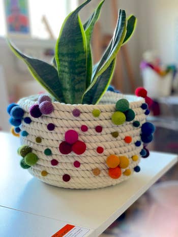 the pot that with beige cotton rope and colorful pom-poms. It's shaped like a vertical cylinder. 