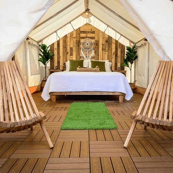 Luxury glamping tent interior with a bed, wooden flooring, two chairs, and decorative plants for a cozy retreat