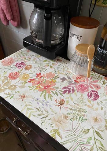 Floral-patterned counter organizer with a coffee maker, a labeled coffee canister, and a glass sugar jar with a wooden spoon on a kitchen countertop
