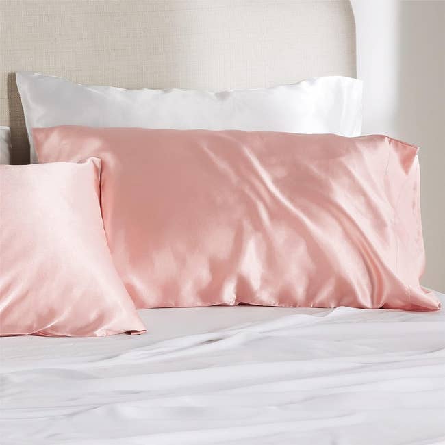 two pillows in coral silk pillowcases on a bed