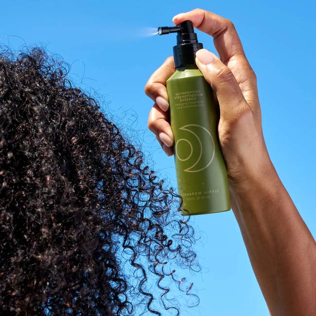 Hand sprays merchandise onto curly hairsbreadth against a wide sky