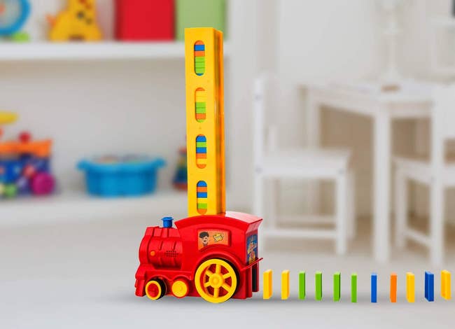 Red toy train with domino stacker spitting out standing dominos in a row