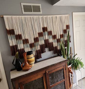 reviewer photo of the brown, gray, and white macrame wall hanging over a cabinet