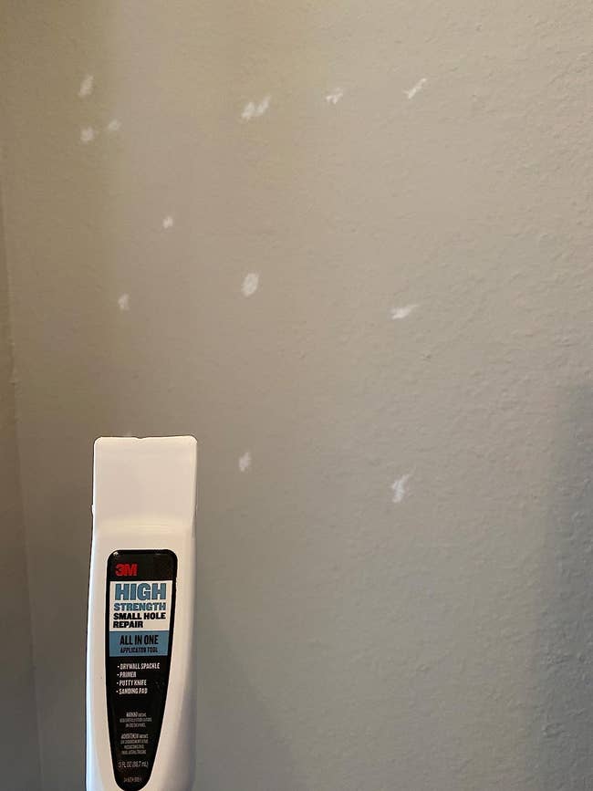 a reviewer holding the tool up against a wall where several holes were repaired 