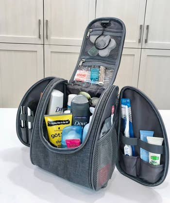 the toiletry bag in gray stuffed with various beauty products 