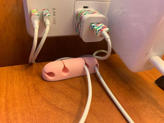 A small pink cable organizer mounted on a desk with cables pinched into it from an outlet 