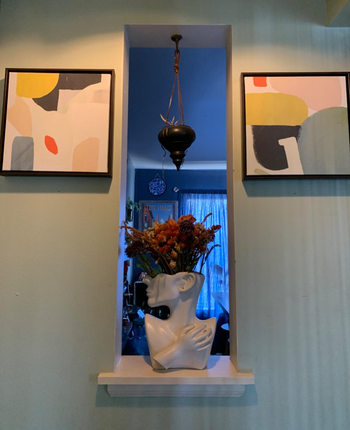 the vase holding flowers in an entryway between to paintings