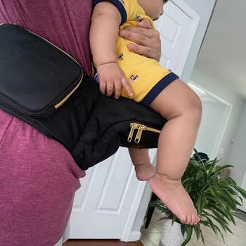 reviewer wearing the hip carrier while holding baby
