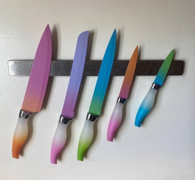 Five kitchen knives with multicolored handles and blades mounted on a magnetic strip
