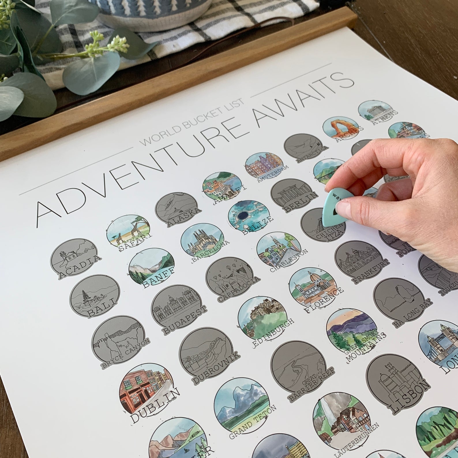 the white poster with circular illustrations of places around the world and a hand scratching one to show the beautiful colors that appear