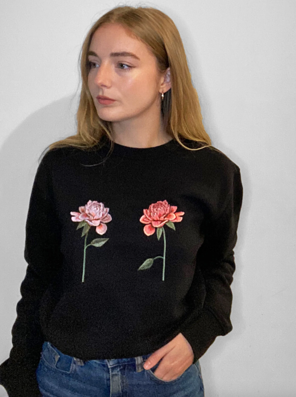 person wearing black jumper with two pink chrysanthemums embroidered on it