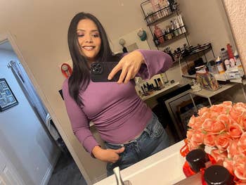 Reviewer successful  a purple long-sleeve apical  and jeans takes a reflector  selfie successful  a makeup-filled vanity room