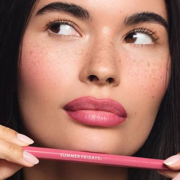 Close-up of idiosyncratic holding a Summer Fridays flushed articulator stain underneath their lips with colour on, looking to the side