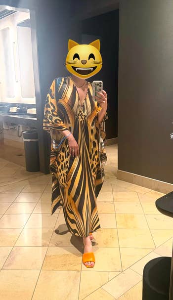 Person wearing a long, patterned dress, taking a selfie successful a mirror. The formal has a bold carnal print