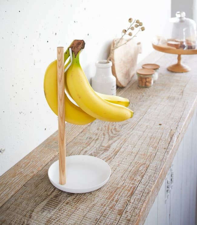 white and wood stand with three bananas hanging from branch
