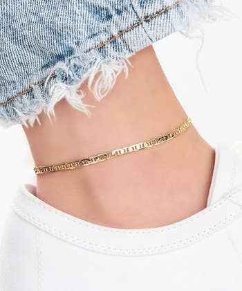 A close-up of an ankle wearing a stylish gold anklet with a chain design