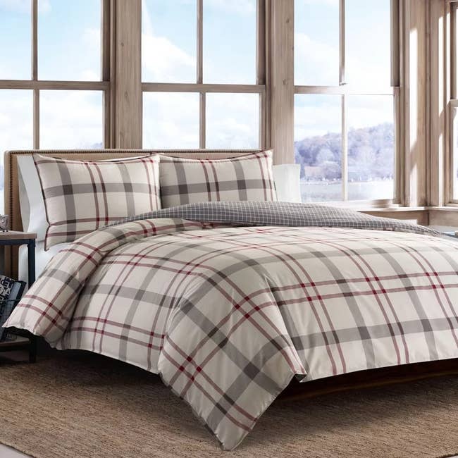 red, white, and gray plaid comforter with matching pillows on a dark wooden bed frame in front of three glass windows