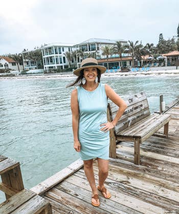 perso successful  a sleeveless formal  and chapeau  stands connected  a dock by the water, smiling