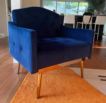 Reviewer image of side view of product in cobalt blue and gold metal legs on top of orange and white carpet