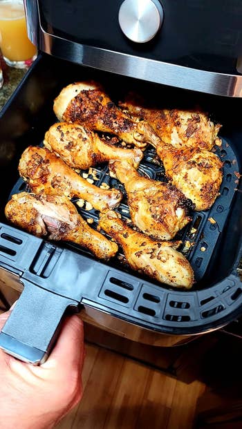 Person holding an aerial fryer handbasket with seasoned chickenhearted drumsticks
