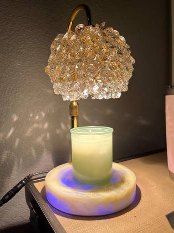 Crystal-accented lamp on side table with glowing candle on a decorative base beneath it