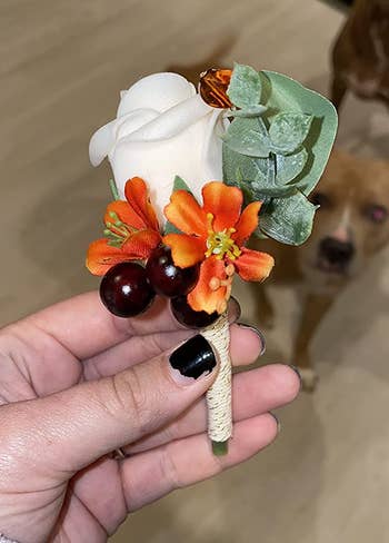 a reviewer holding one of the boutonnière in white with orange and green accents 