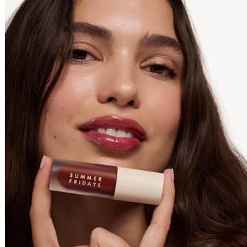 Person holding a conduit of Summer Fridays articulator gloss adjacent their face, showing glossy lips, suitable for a quality oregon buying article